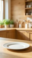 Empty white plate on wooden kitchen counter with natural light, potted plant, and blurred cabinetry in background for dining and food styling.