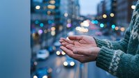 Hands cupped in prayer or meditation gesture against blurred city lights at dusk. Concept of hope, spirituality, and urban mindfulness during evening hours.