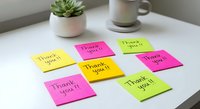 Colorful thank you sticky notes arranged on white desk with succulent plant and coffee mug for gratitude expression and office organization.
