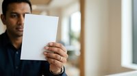 Young man of South Asian descent holding blank white card in modern office environment, suitable for business communications and corporate messaging.