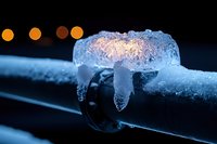 Frozen ice formation on metal pipe with crystalline structure glowing in blue light against dark background, bokeh lights create atmospheric winter mood.