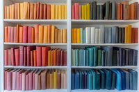 Colorful books arranged by spectrum on white bookshelf, creating rainbow gradient from warm reds and oranges to cool blues and purples.