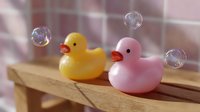 Yellow and pink rubber ducks on wooden surface with floating soap bubbles creating playful bathroom decor composition in soft pastel colors.