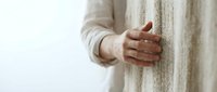 Woman in cozy beige sweater touching textured wall with gentle hand gesture in soft natural lighting for interior design and wellness concepts.