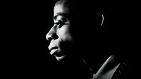 Profile portrait of young African American man in dramatic black and white lighting against dark background, showing contemplative expression and strong facial features.