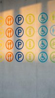 Colorful accessibility and service icons on concrete wall with natural sunlight shadows creating modern wayfinding signage for public spaces and buildings.