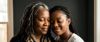 African American mother and daughter embracing warmly in natural light, showing intergenerational love and family bond in intimate portrait setting.