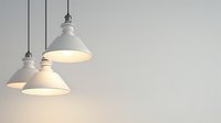 White industrial pendant lamps hanging from ceiling against light gray wall, emitting warm glow. Modern minimalist interior lighting design creates cozy atmosphere.