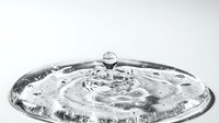Water drop creating ripples in clear liquid with splash crown formation captured in high-speed photography on white background for science education.
