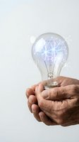 Hands holding glowing light bulb with electric sparks inside representing innovation, creativity and bright ideas for business solutions.