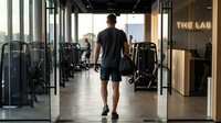 Athletic man walking into modern fitness center carrying gym bag ready for workout session in contemporary health club facility.