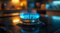 Blue gas flame burning on kitchen stove burner with bokeh lights in dark background, close up view showing energy consumption and cooking concept.