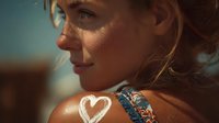 Profile of young Caucasian woman with freckles and blonde hair in warm sunset light, showing heart-shaped sunscreen and tan lines on shoulder.