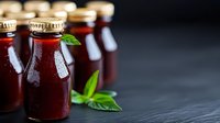 Glass bottles of homemade berry juice or smoothie with fresh basil leaves on dark slate background, perfect for healthy lifestyle content.