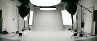Professional photography studio setup with white cyclorama backdrop, studio lighting equipment, softboxes and tripods for commercial photo shoots.