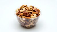 Mixed nuts assortment in glass bowl with almonds, walnuts, pecans and cashews for healthy snacking and cooking on white background.