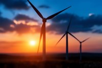 Wind turbines silhouetted against dramatic orange and blue sunset sky. Renewable energy farm with multiple windmills generating clean power at dusk.