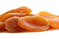Sweet dried apricots arranged in row on white background, showing natural texture and vibrant orange color. Healthy organic snack food photography.