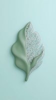 Sage green leaf sculpture with intricate white lace pattern detailing on feathered sections, isolated on soft mint background for decorative design and artistic projects.