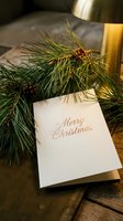 Merry Christmas greeting card with gold script on wooden table, pine branches, cones, and warm lamp light creating cozy holiday atmosphere.