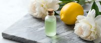 Lemon essential oil in glass bottle with fresh lemons and white peonies on marble surface for spa, wellness and aromatherapy product design.
