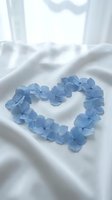 Blue hydrangea petals arranged in heart shape on white silk fabric for romantic wedding decoration and love concept.