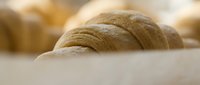 Freshly baked round loaf of artisan bread with golden-brown crust resting on white surface, suitable for bakery, food, and culinary content.