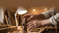 Senior craftsman hands working with traditional woodworking tools in warm workshop lighting creating handmade furniture pieces.