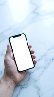 Hand holding a smartphone with blank white screen over marble background, mockup for app or website display presentation.