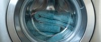 Teal towels inside a front-loading washing machine drum, close-up view of laundry care and household cleaning routine.