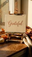 Grateful canvas on wooden easel with autumn pumpkins and cozy blanket in warm sunlit room for Thanksgiving home decor and seasonal interior design.