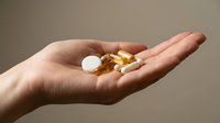 Caucasian adult hand holding assorted pharmaceutical pills and capsules against neutral background for healthcare, medicine, and wellness concepts.