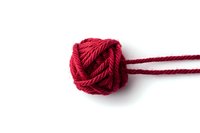 Red wool yarn tied in decorative knot against pure white background, isolated macro shot showing detailed texture of twisted fiber strands.