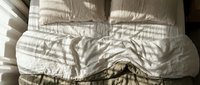 Unmade bed with white rumpled sheets and pillows, showing wrinkled fabric texture and natural morning light casting shadows for bedroom, hospitality, or lifestyle content.