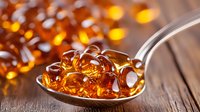 Fish oil omega-3 supplements in spoon on wooden background with scattered golden capsules, soft focus and warm lighting creates appetizing glow.