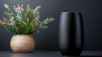 Minimalist black ceramic vase and beige pot with pink wildflowers on dark background. Modern home decor composition with dramatic lighting and soft focus.