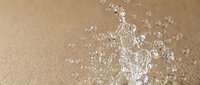 Water splash with droplets on beige sandy background creating refreshing summer concept for beverage advertising and wellness campaigns.