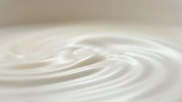 Smooth white cream or milk swirling in circular motion, creating ripple patterns and waves across surface for cosmetics, dairy, or skincare product backgrounds.