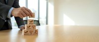 Businessman stacking wooden blocks with customer service icons on office desk representing quality management and business excellence strategy.