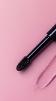 Black mascara wand with brush applicator on pink background with smudged makeup trace, minimalist cosmetic flatlay composition for beauty and makeup concepts.