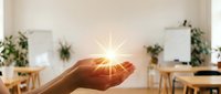Young adult hand holding glowing light orb in modern office workspace with plants and natural sunlight, representing innovation, success, and sustainable business growth.
