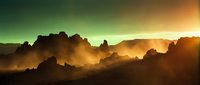 Dramatic mountain landscape with golden sunrise light breaking through dark storm clouds and mist, creating atmospheric layers of silhouetted peaks and glowing sky for nature and travel projects.