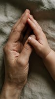 Adult and child hands touching in prayer position showing family bond, protection and care concept with warm natural lighting on textured fabric background.