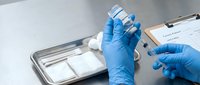 Medical professional in blue gloves preparing vaccine injection from vial on sterile tray in clinical laboratory setting for immunization program.