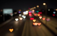 Blurred city street at night with heart-shaped bokeh lights creating romantic atmosphere. Urban traffic and colorful illumination for Valentine's Day designs.