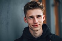 Young Caucasian man with brown hair smiling confidently in black hoodie against urban background for lifestyle and portrait photography projects.