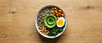 Healthy Buddha bowl with quinoa, chickpeas, avocado rose, boiled egg and greens on wooden table. Nutritious vegetarian meal for balanced diet and wellness.