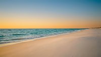 Serene ocean waves gently washing onto pristine sandy beach during golden hour sunset with peaceful turquoise waters and warm glowing sky for relaxation.