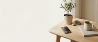 Minimalist wooden table with smartphone, coffee cup, notebook and small potted plant in modern neutral interior space for workspace design.