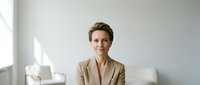 Professional middle-aged Caucasian businesswoman in beige blazer smiling confidently in modern office interior for corporate and business presentations.